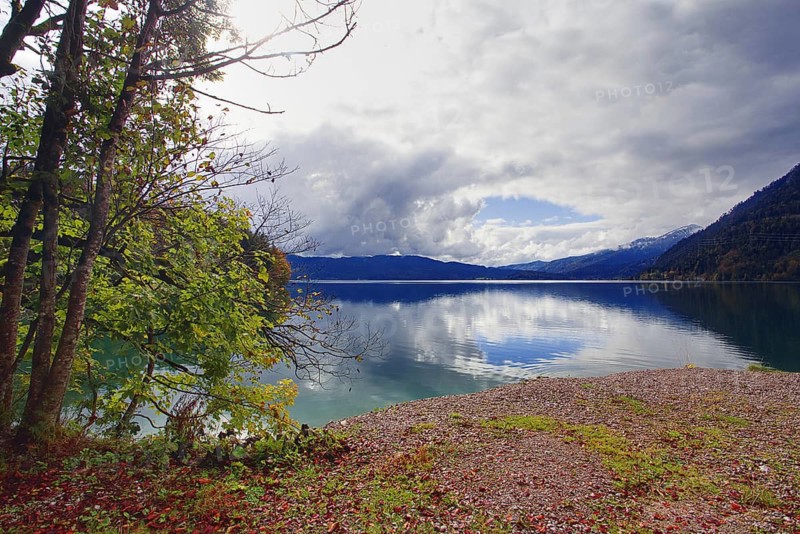 Large lake with pebble beach and cloudy reflection in front of a mountain backdrop, Walchensee, Kochel am See, Bavaria, Germany