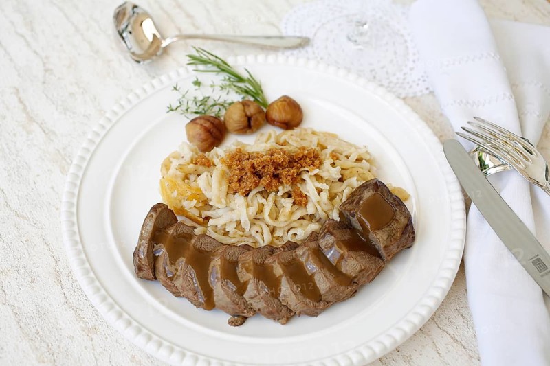 Swabian cuisine, roast venison with spaetzle, chestnuts and breadcrumbs, breadcrumbs, saddle of venison arranged on a plate, gravy, game dish, meat, main course, gravy, cutlery, knife, fork, grandmother's kitchen, regional, home cooking, typical Swabian, traditional cuisine, festive tablecloth, food photography, studio, Germany