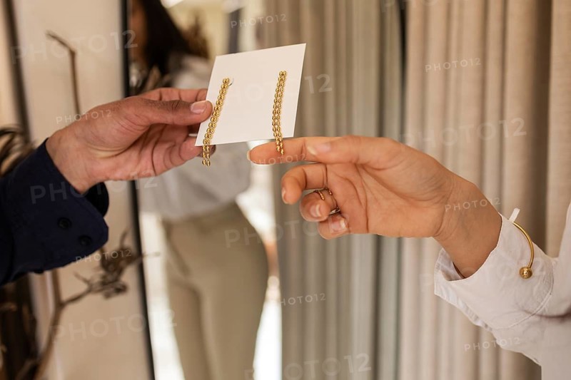A customer exchanges elegant drop earrings with a sales assistant in a modern, well lit boutique. The atmosphere reflects luxury and refined shopping experiences
