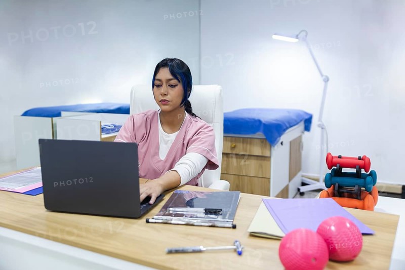 An Ecuadorian physiotherapy clinic features a therapist working at a desk with rehabilitation equipment nearby. The setting highlights a professional healthcare environment