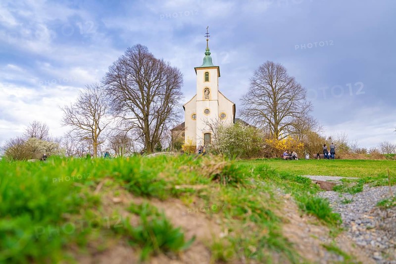 Church surrounded by a green meadow with bare trees and a cloudy sky. Spring-like atmosphere, Michelsberg, Bad Münstereifel