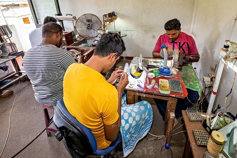 Several people work concentrated on pieces of jewelry with various tools in a workshop. The sapphire and gemstone cutters near Ratnapura in Sri Lanka