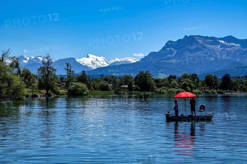 Angler auf Boot, Sonnenschirm, rot, im Hintergrund Schweizer Alpen, Titlis, Pilatus, Sempachersee, Sempach, Kanton Luzern, Schweiz