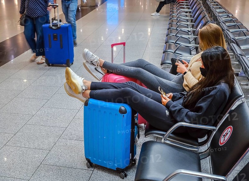 Düsseldorf, North Rhine-Westphalia, Germany - Düsseldorf Airport, start of the holidays in North Rhine-Westphalia, young woman sitting in the departure hall, their legs relaxed on their suitcases, waiting to take off on their summer holidays in times of the corona pandemic