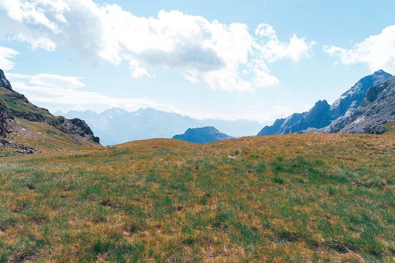Captivating landscape of the Ibones de Anayet in Huesca, Spain, showcasing lush grasslands against a backdrop of majestic mountain ranges under a partly cloudy sky