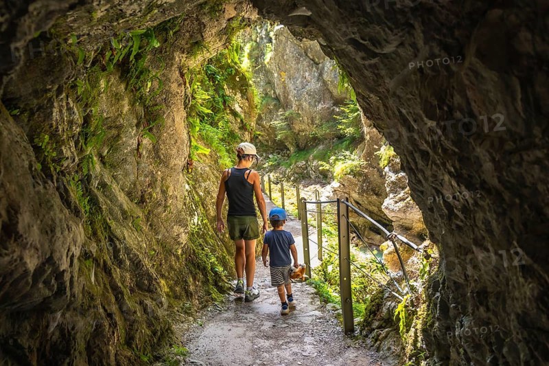 Mother and son walking through a narrow passage carved into the rock face at tolmin gorge in slovenia, enjoying a summer day exploring nature