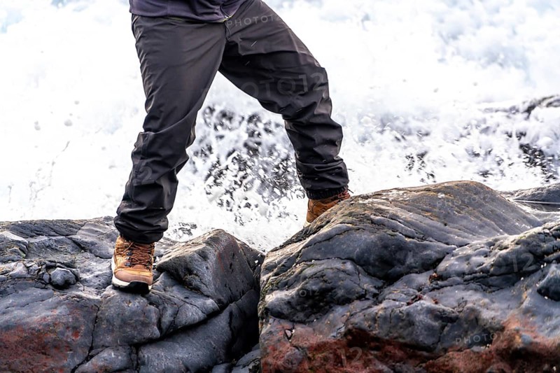 A person is standing on a rock near a body of water. The person is wearing a brown jacket and brown pants
