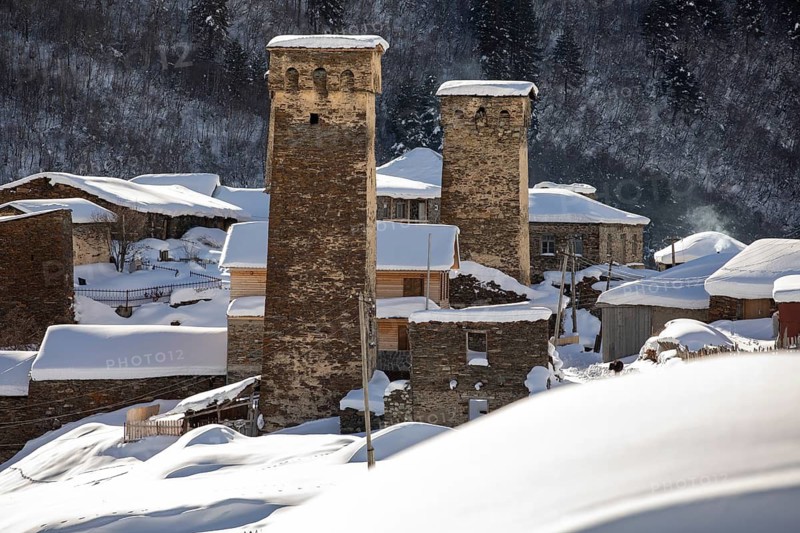 Majestic stone towers covered in snow stand amid a serene winter landscape, showcasing historical architecture and tranquil natural surroundings in Georgia Trees blanket the backdrop