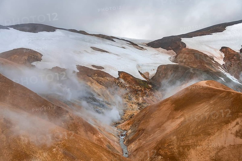 Steaming stream between colourful rhyolite mountains and snowfields, Hveradalir geothermal area, Kerlingarfjöll, Icelandic Highlands, Iceland