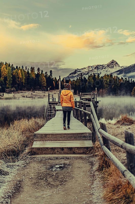 Young woman at Lake Staz near Sankt Moritz in the Engadine in Switzerland. Morning atmosphere with fog in autumn. Reflection of water