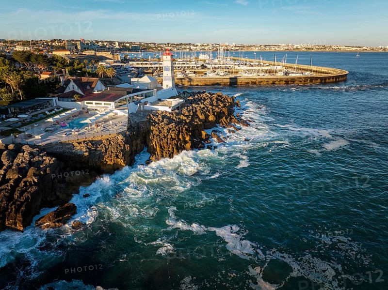 Aerial view of Santa Marta lighthouse and Cascais marina with moored yacht boats with Cascais cityscape, Portugal on sunset