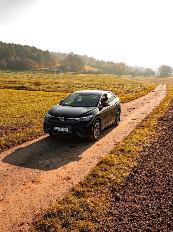 A car on a country lane, flanked by green fields in the early morning light, electric car VW ID5, Deer Carsharing, Gechingen, Black Forest, Germany