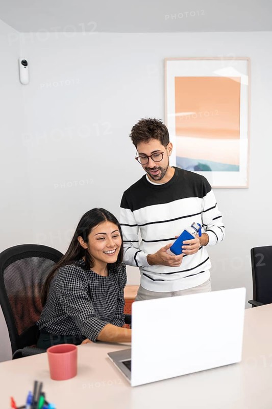 Two coworkers collaborate in an office setting, focused on a laptop screen They engage in teamwork, sharing ideas and solutions The workspace is modern and bright