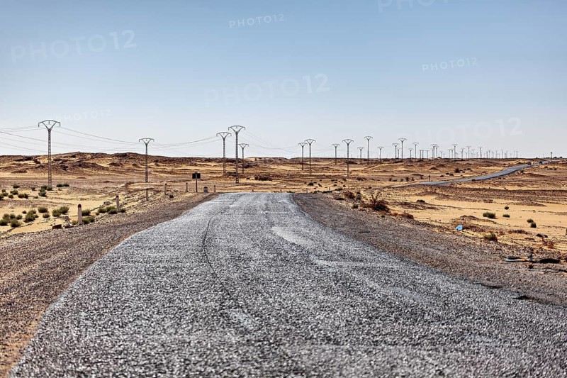 Long road through the desert with numerous electricity pylons stretching to the horizon, By car through the Sahara desert in Algeria