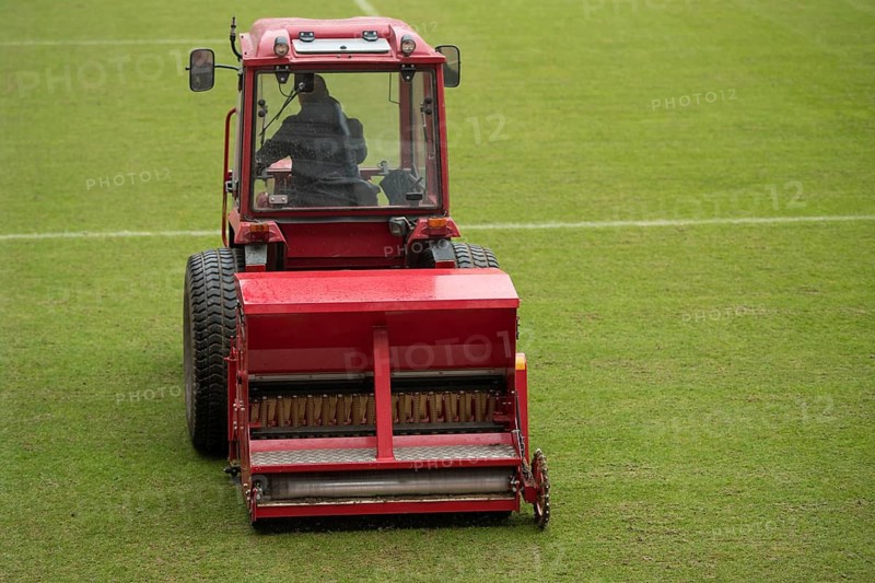 A man in a tractor with a disc seeder drill sowing grass on a football field in Lubin, Poland