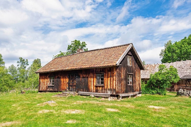 Old idyllic wooden cottage on a meadow with an old barn in a historic old rural setting in summer, Sweden