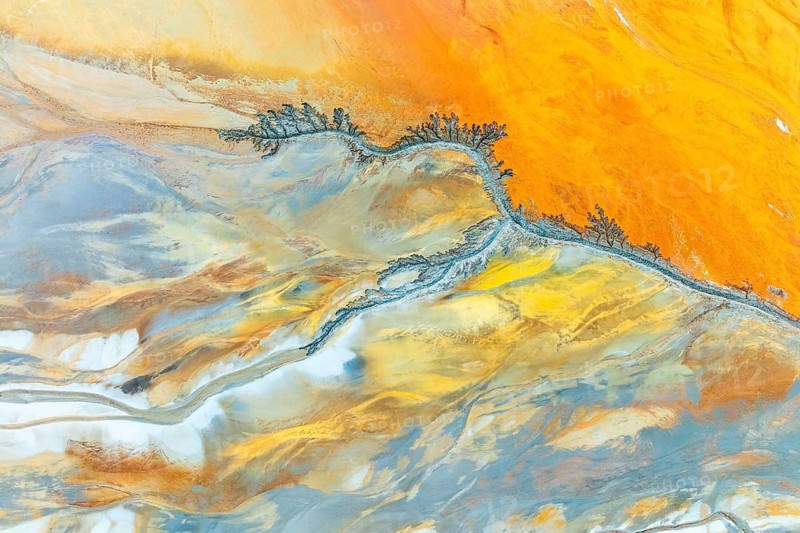 This aerial view captures intricate fractal mud patterns with vibrant orange and blue hues, creating a mesmerizing abstract landscape. Perfect for backgrounds and artistic designs