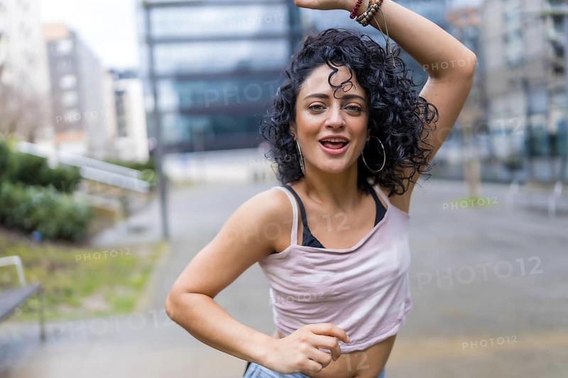 Curly haired dancer joyfully performing in a bustling city street, radiating energy and passion while embracing the vibrant urban lifestyle