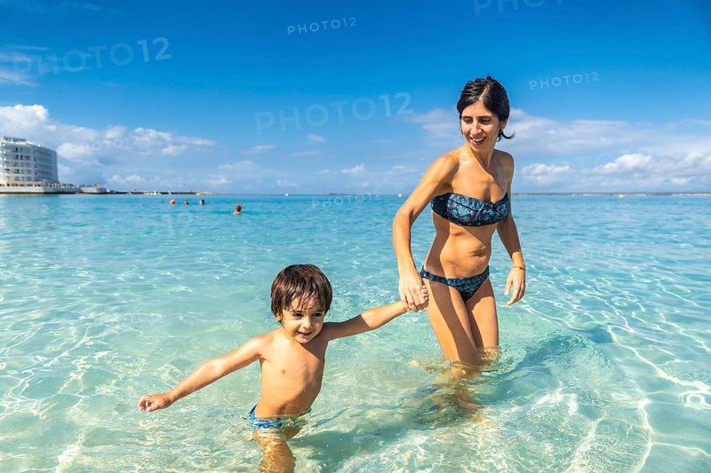 A woman and a child are playing in the ocean. The woman is holding the child's hand