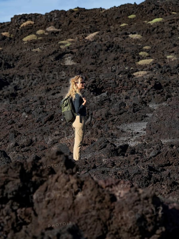 A woman explores the rugged volcanic terrain of Timanfaya National Park in Lanzarote, Canary Islands, Spain. The scene captures the stark beauty of the volcanic landscape
