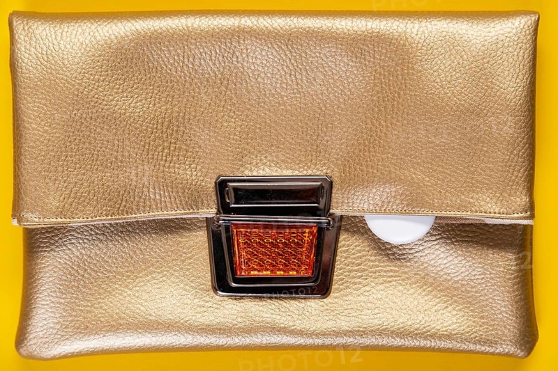 An Apple Air tag lies on a golden faux leather clutch against a plain yellow background