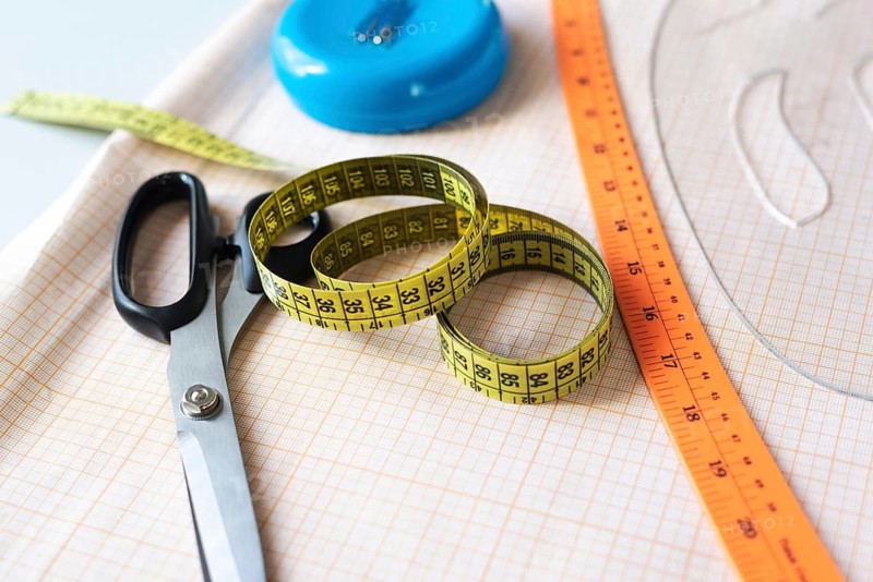 A vibrant collection of sewing essentials including scissors, measuring tape, and a ruler, all thoughtfully arranged on fabric in a workshop setting, evoking creativity and craftsmanship