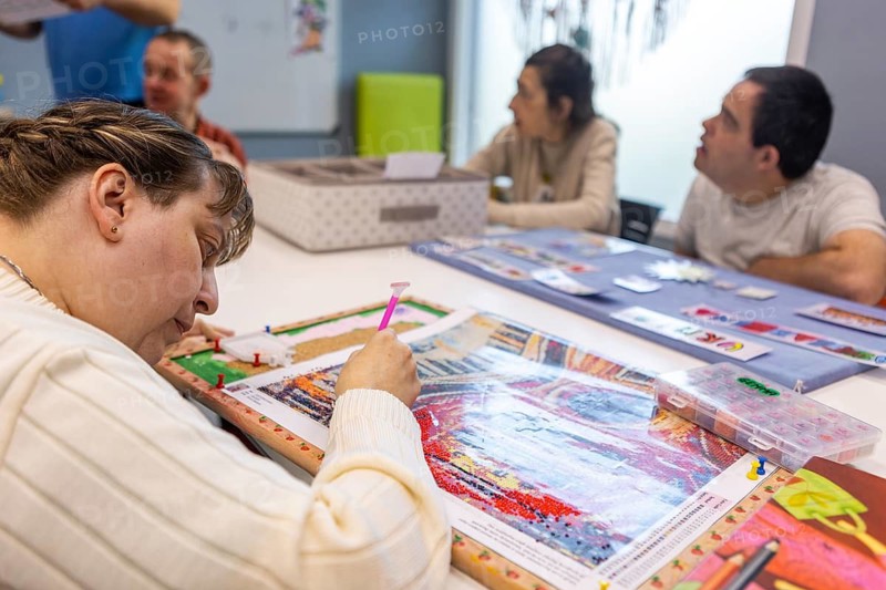 Individuals engaging in creative activities at a mental health day center, focusing on painting and puzzles in a supportive and inclusive environment