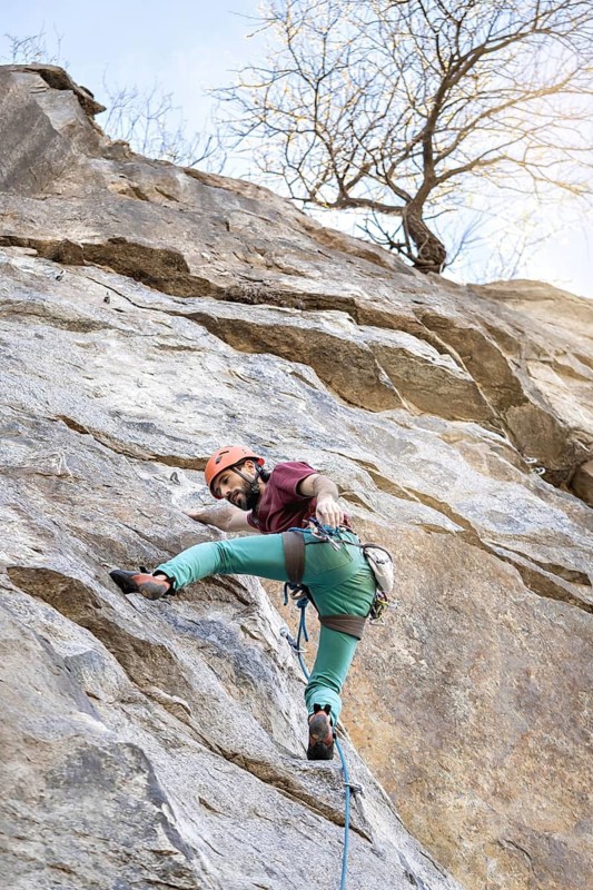 A young man tackles a steep cliff route, exemplifying the thrill and challenge of extreme sports. His focused determination and climbing skills highlight the intensity of the natural rock face
