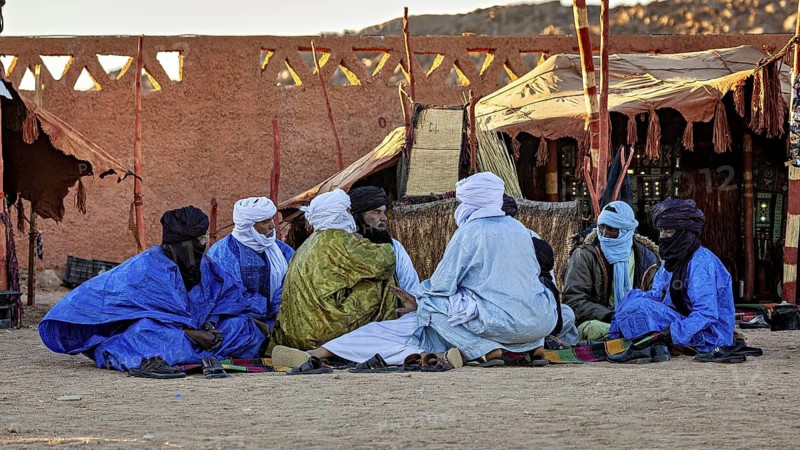 Group of people in traditional dress sitting in front of a tent in the desert, men at the traditional Tuareg festival of Tamanrasset in the Sahara in Algeria