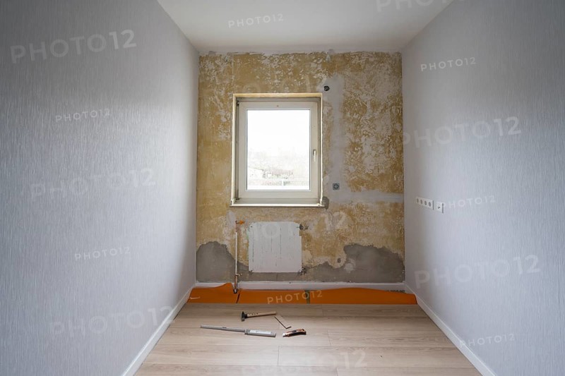 Room is being renovated, partly wallpapered, laminate and tools on the floor