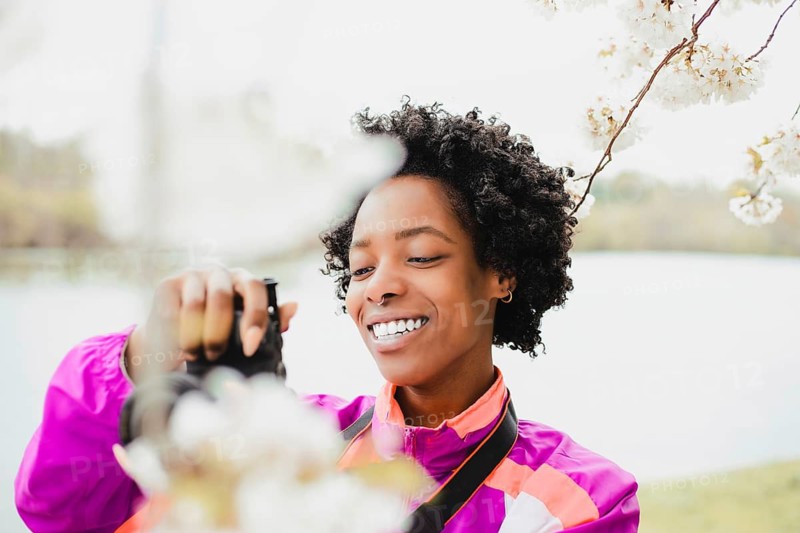 A joyful Black woman photographer, in an outdoor setting, capturing the delicate beauty of cherry blossoms. The image highlights creativity and nature's charm
