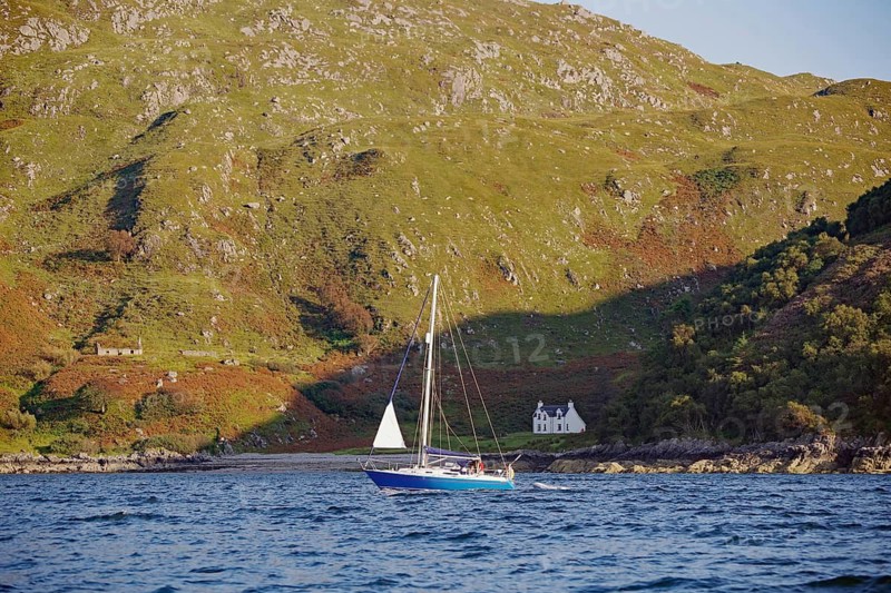 A sailboat sails on water in front of a mountainous landscape with a single house, Mallaig, Scotland, Great Britain