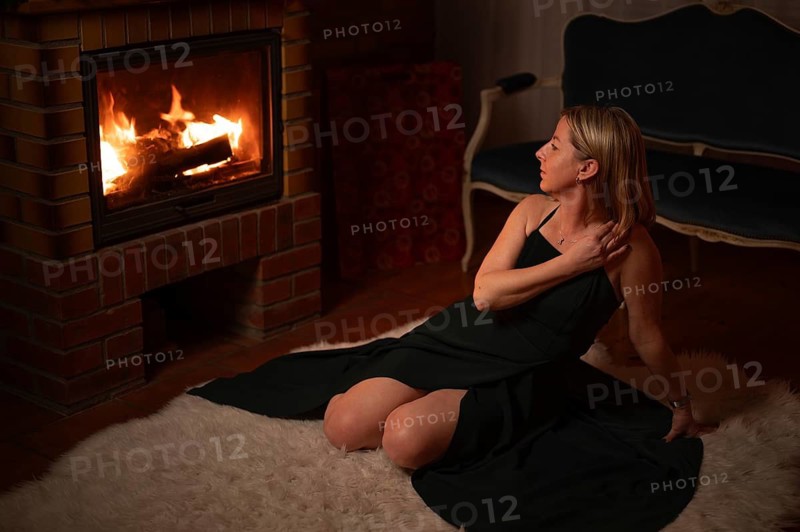 A woman in a dress sitting on a fur coat in front of a fireplace