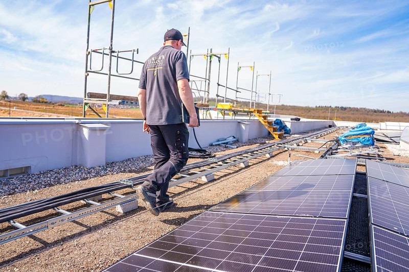 Construction workers on a roof surrounded by solar panels and blue skies, PV installation. OBI Baumarkt, Mühlacker, Enzkreis, Germany
