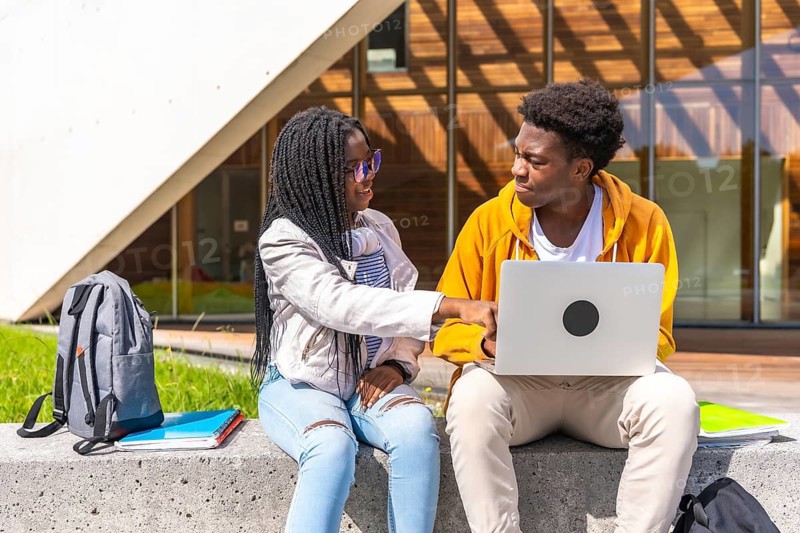 African woman pointing the laptop screen while studying with a male colleague in the campus of the university