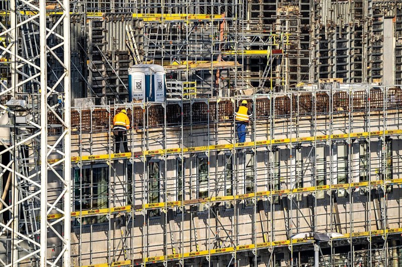 Large construction site, scaffolded new building, factory and office building, workers on the scaffolding during facade work