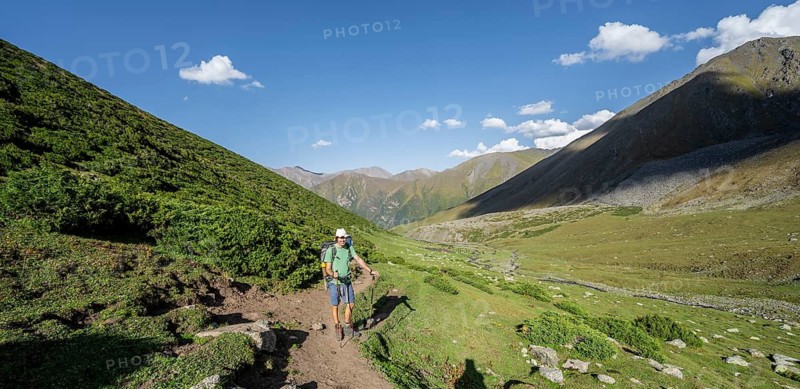 Mountaineers on a hiking trail, green high valley with mountain stream, Keldike Valley on the way to the Ala Kul Pass, Tien Shan Mountains, Kyrgyzstan