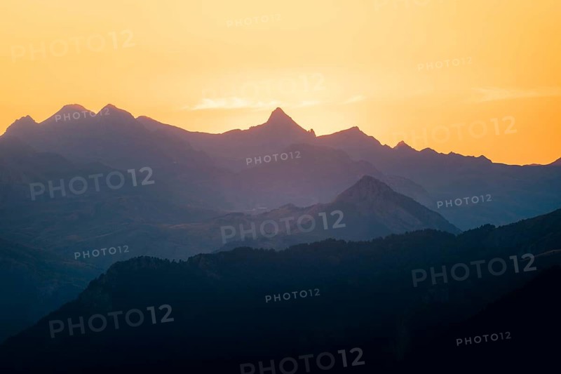 Serene image capturing silhouette of mountains at golden sunset in the Pyrenees. Layers of peaks create a calming, natural scene, with softly changing colors in the evening sky