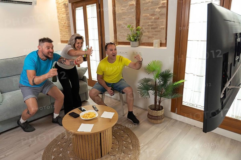 Excited friends standing up and cheering during a live sports match on television. High energy, positive emotions, teamwork and entertainment at home