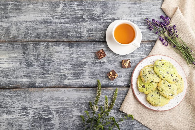 Green cookies with chocolate and mint on ceramic plate with cup of green tea and linen textile on gray wooden background. top view, flat lay, copy space