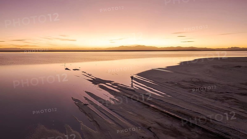 A solo traveler at a mesmerizing sunset in Salinas Grandes, Salta, Argentina, where the vast salt flats meet a golden horizon, creating stunning reflections and a tranquil atmosphere