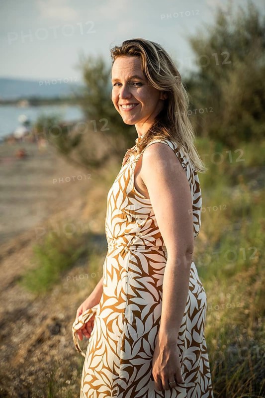 A woman smiles warmly while standing near the beach in Italy. The golden sunlight illuminates her face as she enjoys the fresh breeze and the peaceful coastal surroundings