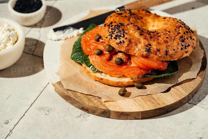 A gourmet bagel topped with smoked salmon, capers, and fresh greens on a wooden platter. The sesame seeds add texture, creating a mouthwatering, savory breakfast option
