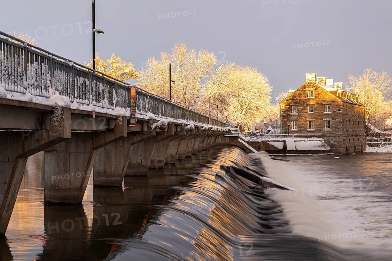 Moulin Neuf water flow control dam and walkway over Des Mille-Iles river plus New Mill on Ile des Moulins with first winter like snow in late autumn at sunset, Old Terrebonne, Quebec, Canada