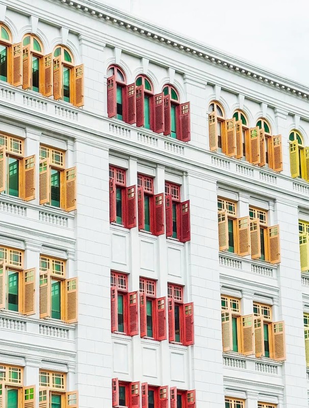 Vibrant red, yellow, and green window shutters contrast against the crisp white facade of a colonial style building in Singapore, showcasing architectural heritage