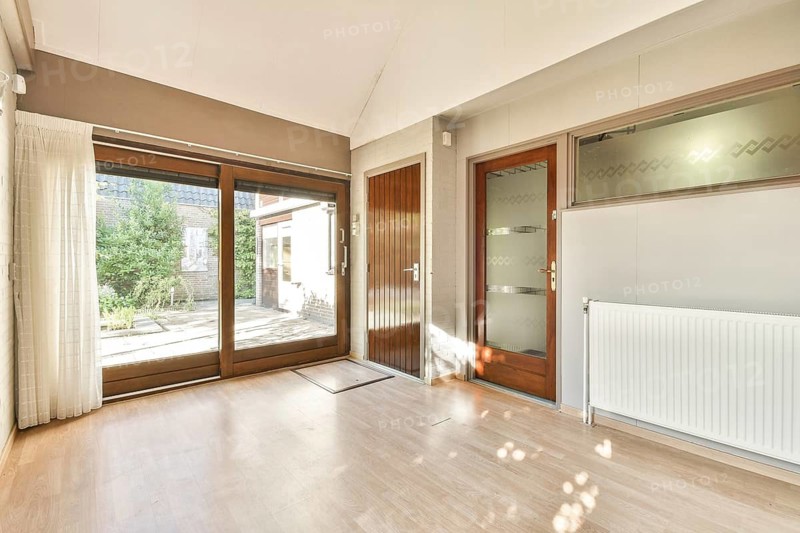 A spacious interior featuring large windows that invite ample natural light, highlighting a minimalist design with wooden floors and smooth walls