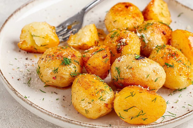 Half-eaten fried new potatoes, with butter and dill, on a white plate, with a fork, at home, no people