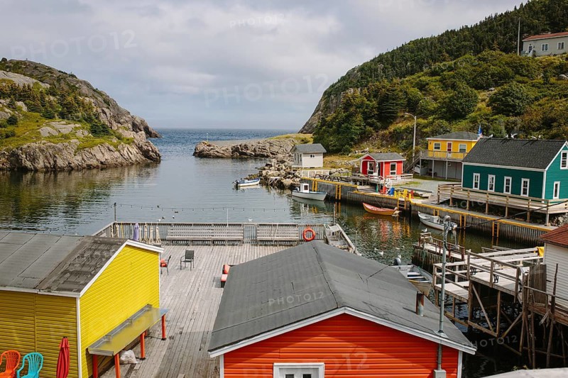 Colorful coastal view of a vibrant waterfront in St. John's, Newfoundland & Labrador. The scene showcases brightly painted buildings, serene water, and rugged landscapes, providing a typical picturesque setting of a Canadian fishing village
