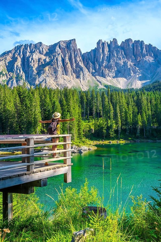 Tourist with open arms enjoying the breathtaking view of lake carezza and latemar mountain range, italian dolomites
