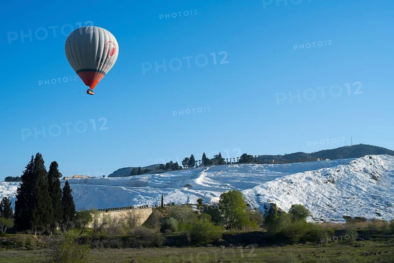 A single hot air balloon flies high above white limestone terraces and trees, sinter terraces, lime sinter terraces, travertine terraces, Pamukkale, Denizli, UNESCO World Heritage Sites, Anatolia, Turkey
